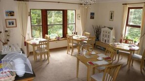 Une salle à manger avec des tables et des chaises en bois, de grandes fenêtres avec des rideaux et un lustre.