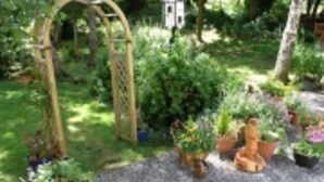 Un jardin agrémenté d’une tonnelle en bois, de plantes en pot et d’une petite construction blanche.