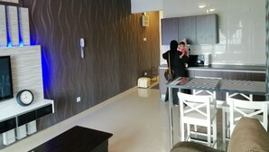 A modern living room with a flat-screen TV, a ceiling fan, and a dining area with white chairs and a glass table. - Lawang Suite 1 Bedroom Corner Apartment (Shah Alam)