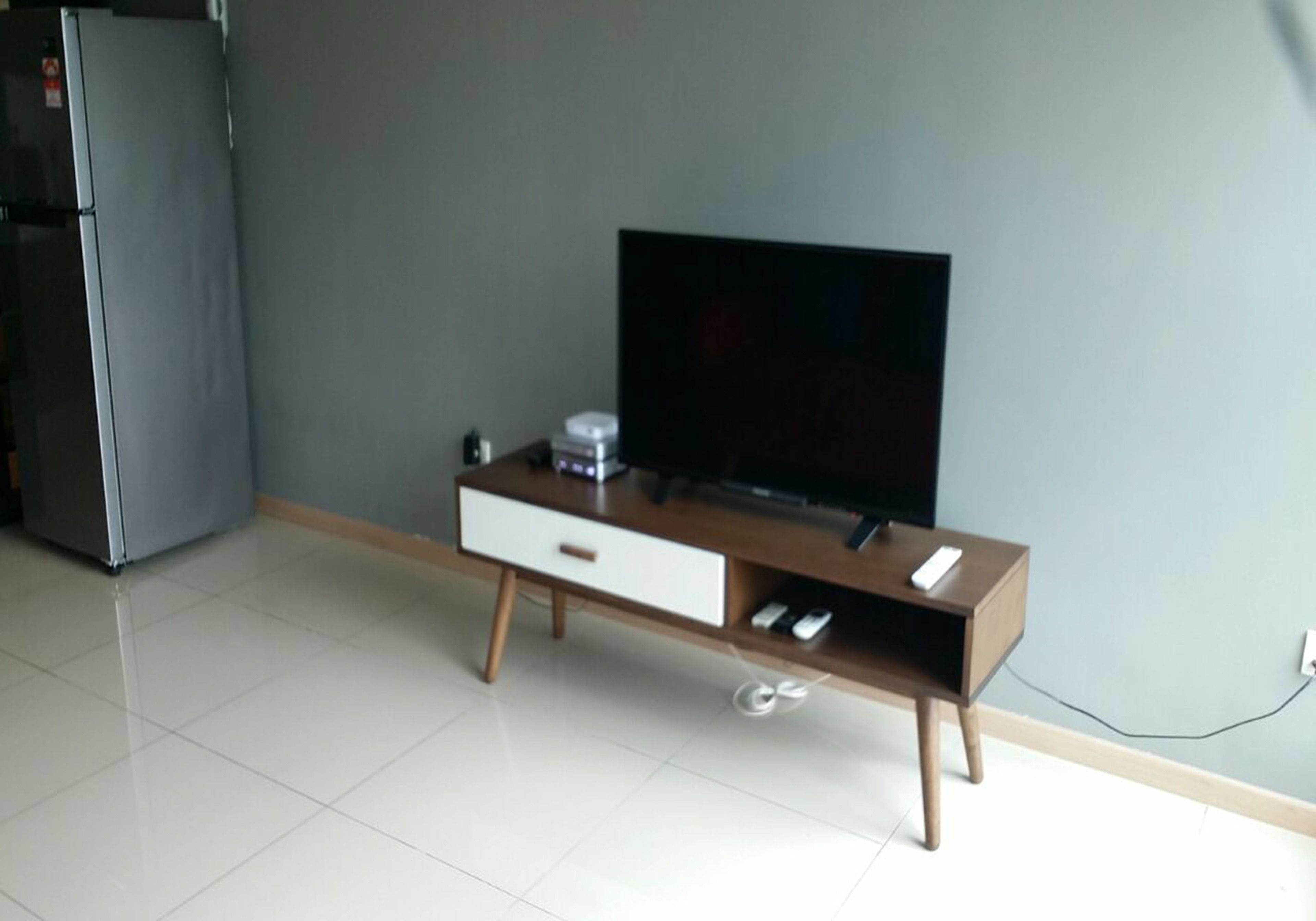 A modern living room with a flat-screen TV on a wooden TV stand, a small white cabinet, and a refrigerator.