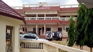 A hotel named "Hotel Villa Des Hotes" with a tiled patio, a balcony with a railing, and several parked cars. - Villa des Hôtes II (Yamoussoukro)