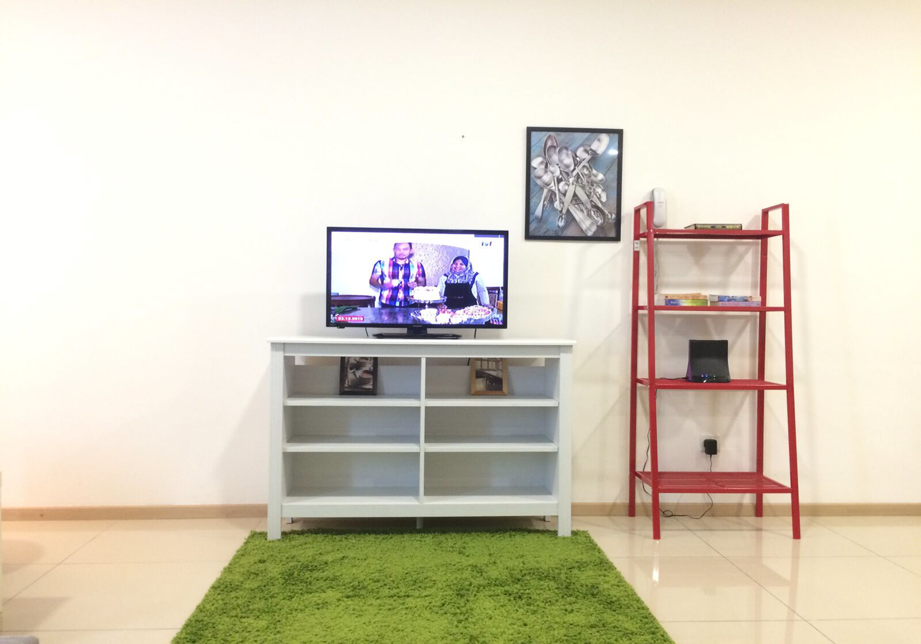 A living room with a television on a white stand, a red bookshelf, and a green rug.