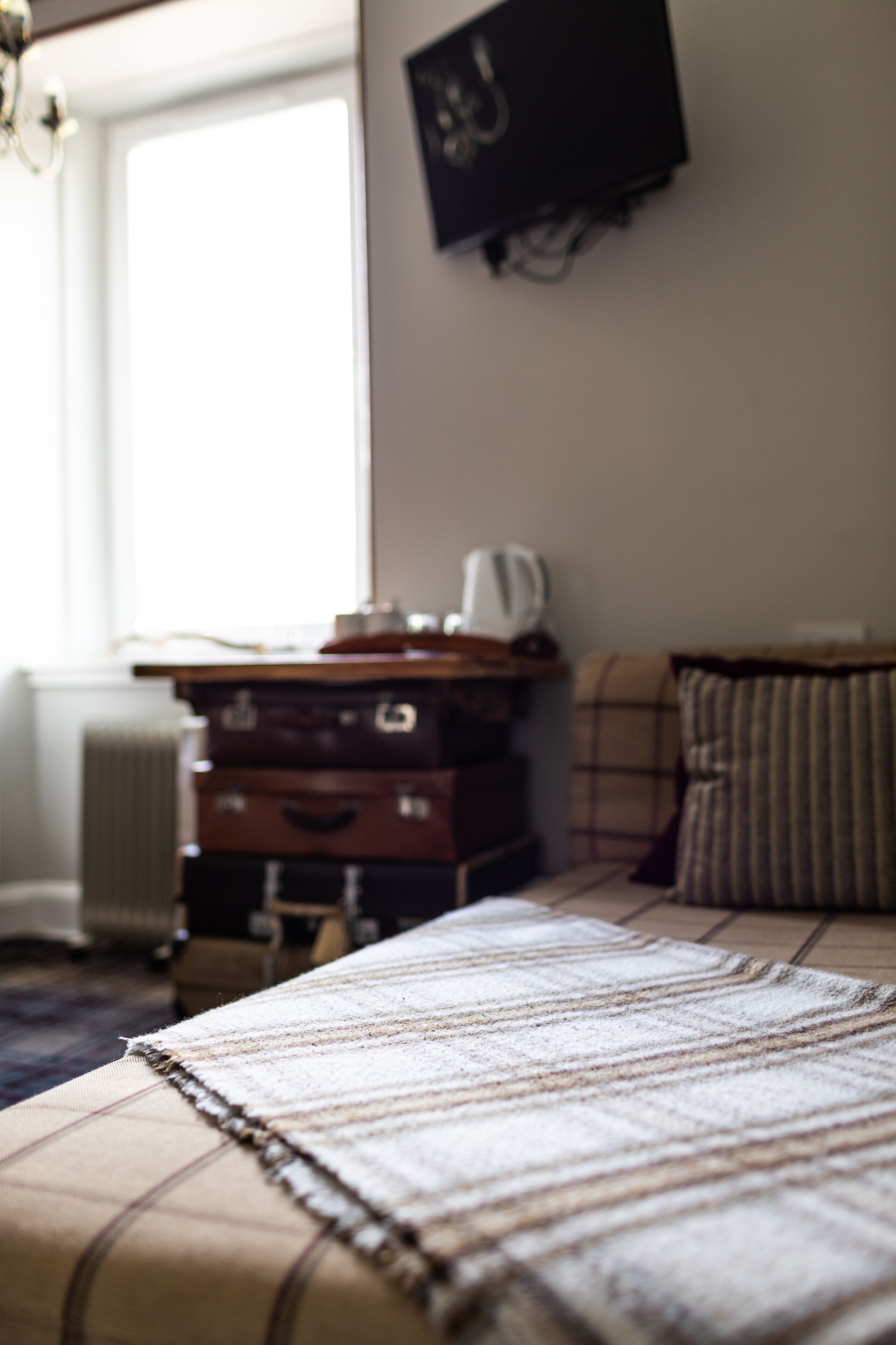 A bedroom with a bed, a radiator, a window, a television, and a dresser.