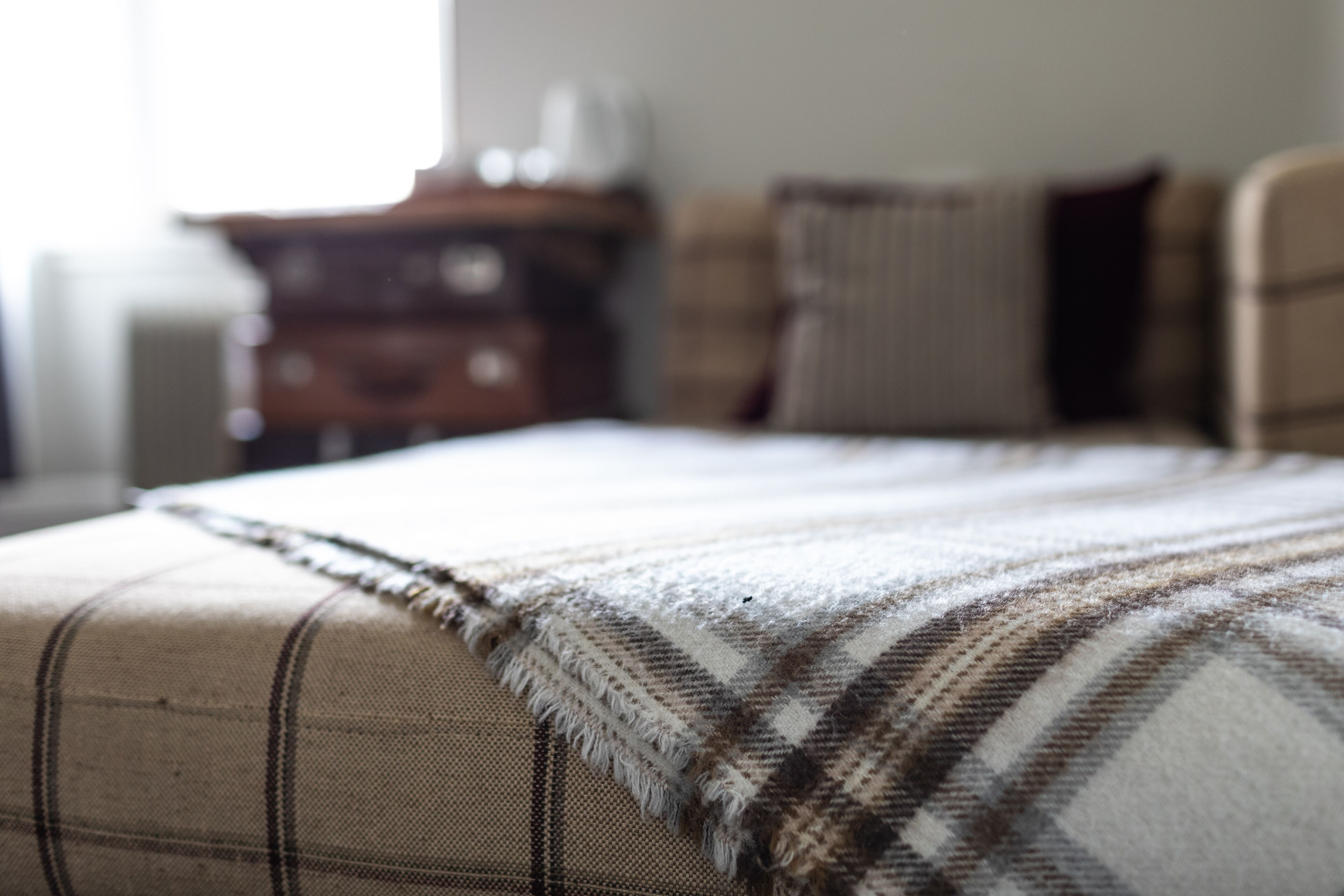 A bed with a plaid blanket and a wooden dresser in the background.