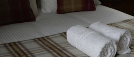 A neatly made bed with plaid bedding, two rolled towels, and a lamp on a bedside table.