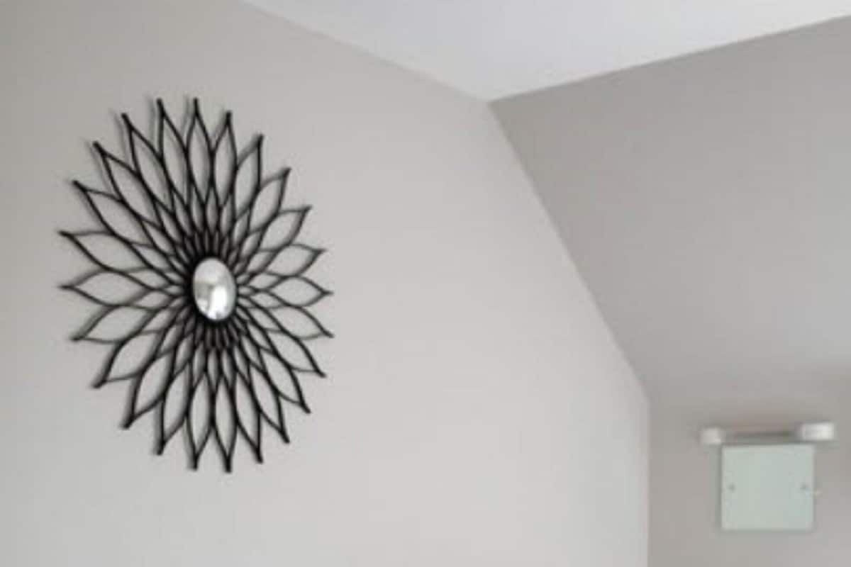 A bedroom with two beds, a bedside table with a lamp, a wall-mounted mirror, and a decorative metal piece.