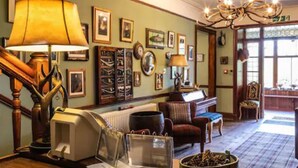 A cozy room with a fireplace, a wooden staircase, and a chandelier. - Whitebridge Hotel (Inverness)