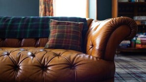 A brown leather sofa with tufted detailing, a plaid throw blanket, and a plaid pillow. - Whitebridge Hotel (Inverness)