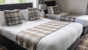 A hotel room with two beds, each with white linens and plaid blankets. There is a bedside table with a lamp and a framed picture on the wall. - Whitebridge Hotel (Inverness)