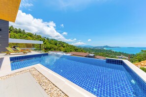 A modern outdoor swimming pool with a view of a coastal landscape and hills. - Samui Villa Bebe (Koh Samui)