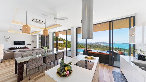 A modern kitchen with a central island, dining area with wicker chairs, and a large window overlooking a scenic view. - Samui Villa Bebe (Koh Samui)