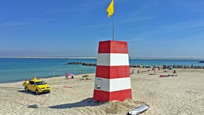 En strand med et rødt og hvidstribet fyrtårn, en gul redningsbåd og en klar blå himmel.
