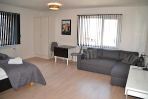 A modern, well-lit room with a bed, a grey sofa, a desk, and a chair. - Thyborøn Hotel (Thyborøn)