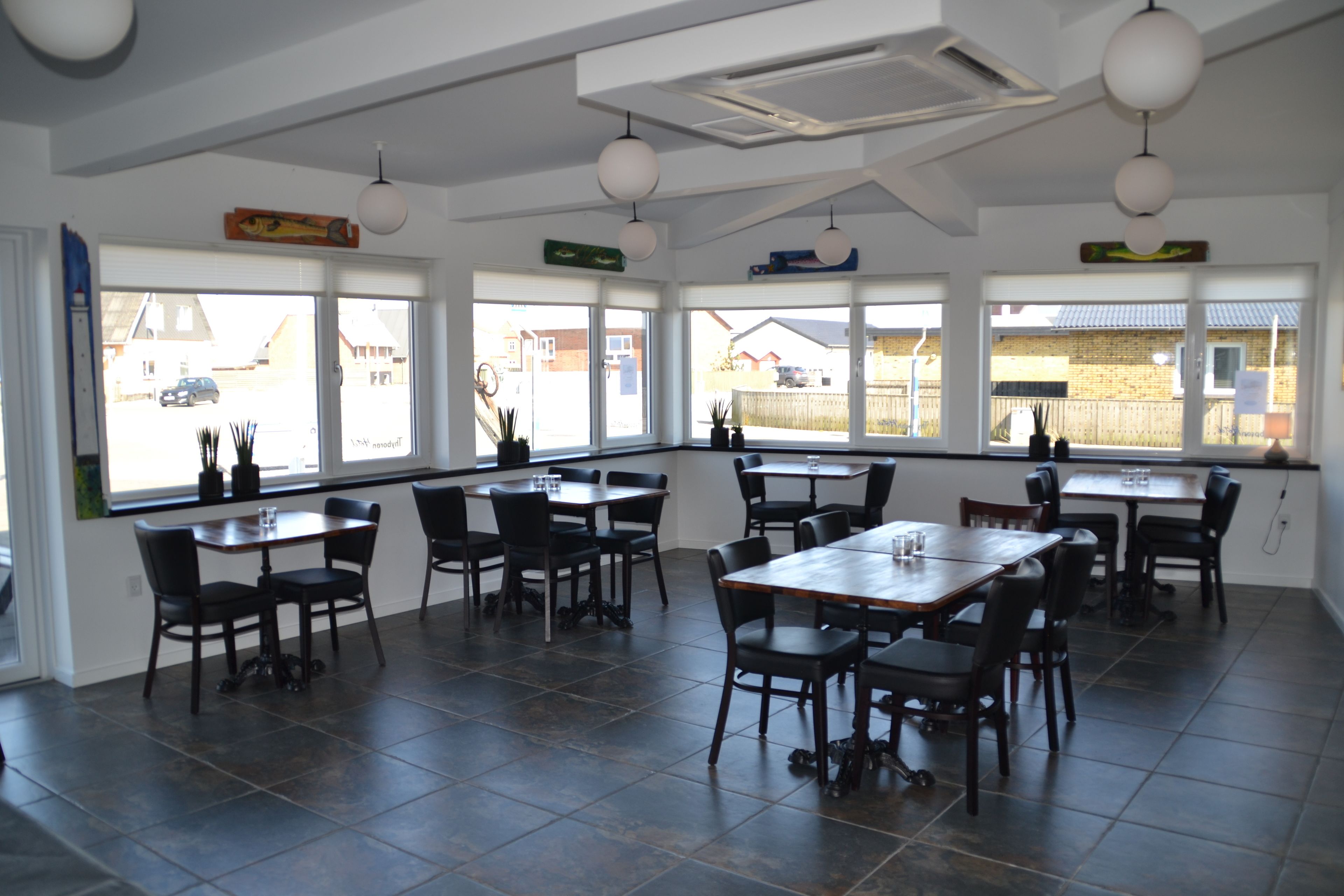 A spacious dining area with multiple tables and chairs, large windows with views of the outside, and a modern ceiling design.