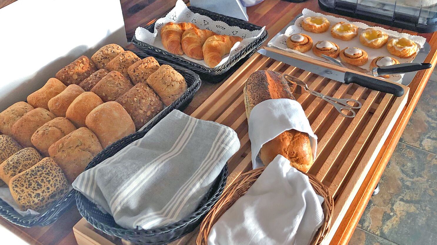 A variety of breads and pastries on a wooden table, including croissants, muffins, and bread rolls.