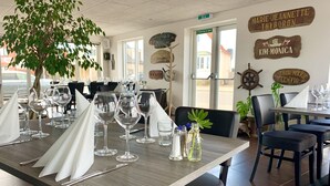En restaurantindretning med et træbord dækket til spisning, stole og en dekorativ plante.