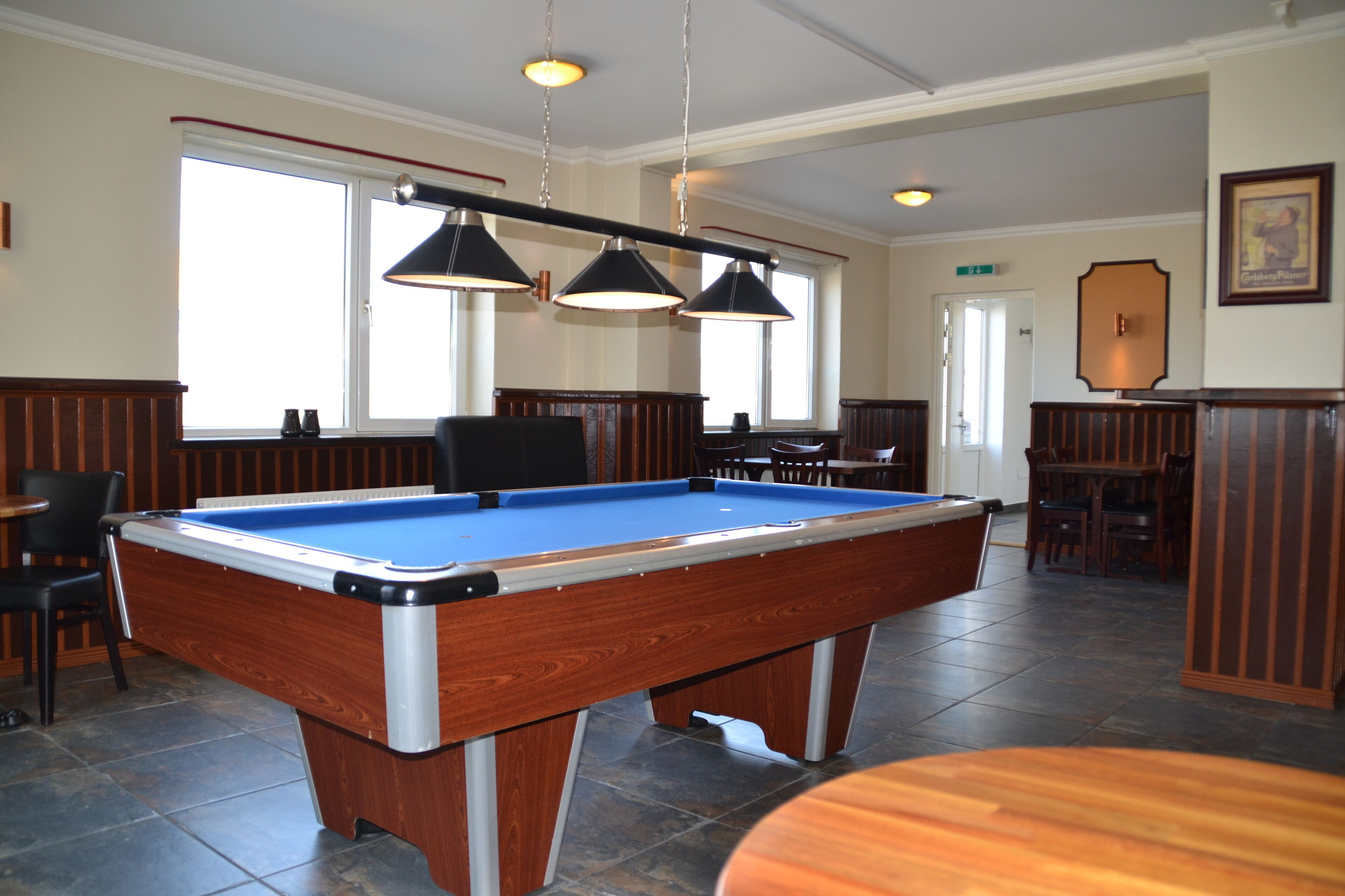 A pool table in a room with a high ceiling, large windows, and wooden paneling.