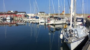 En havn med flere både i havnen, roligt vand og bygninger i baggrunden.