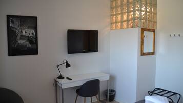 A bedroom with a bed, a desk, a chair, a TV, a mirror, and a window with a view of trees.