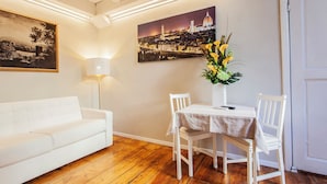 A room with a white sofa, a dining table with two chairs, a vase with flowers, and two wall-mounted paintings. - Hotel St. James (Florence)
