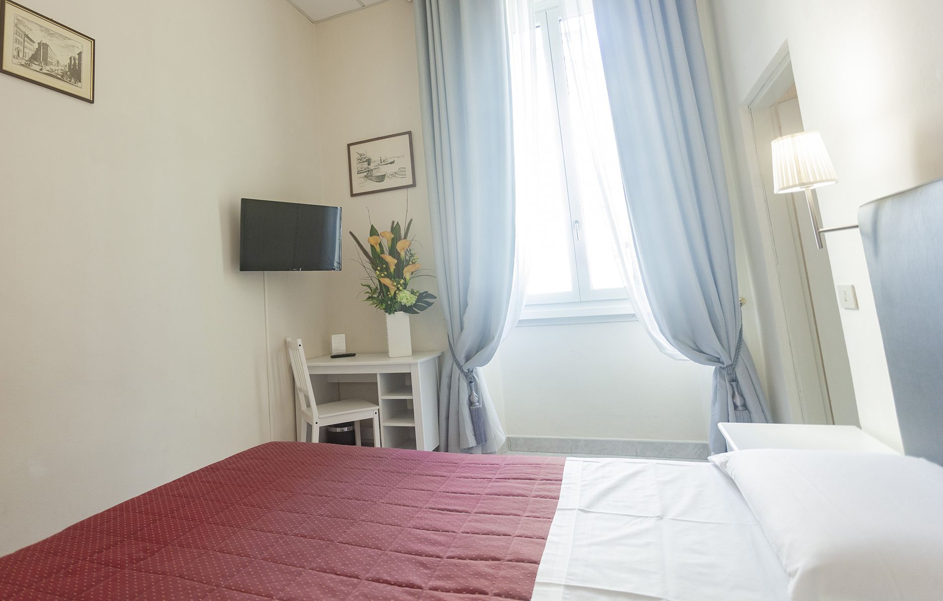 A hotel room with a bed, a desk, a chair, a TV, and a window with curtains.