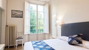 A bedroom with a bed, a chair, a radiator, a window, and a painting on the wall. - Hotel St. James (Florence)