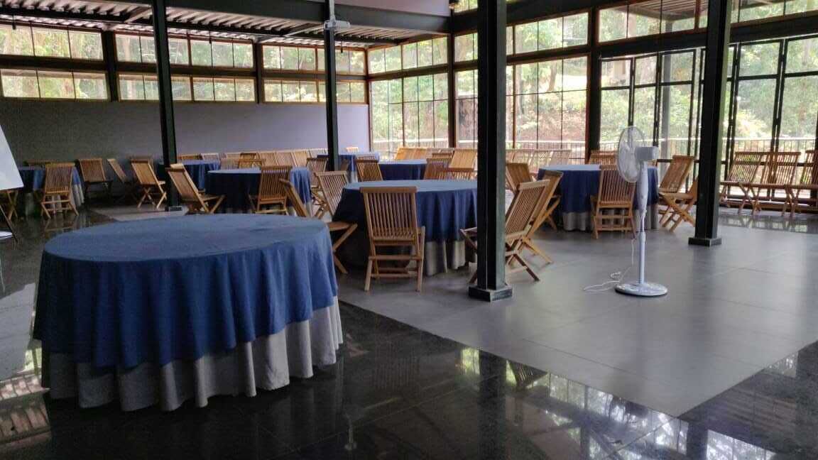A spacious indoor area with round tables covered with blue tablecloths and wooden chairs, large windows providing natural light, and a polished floor.