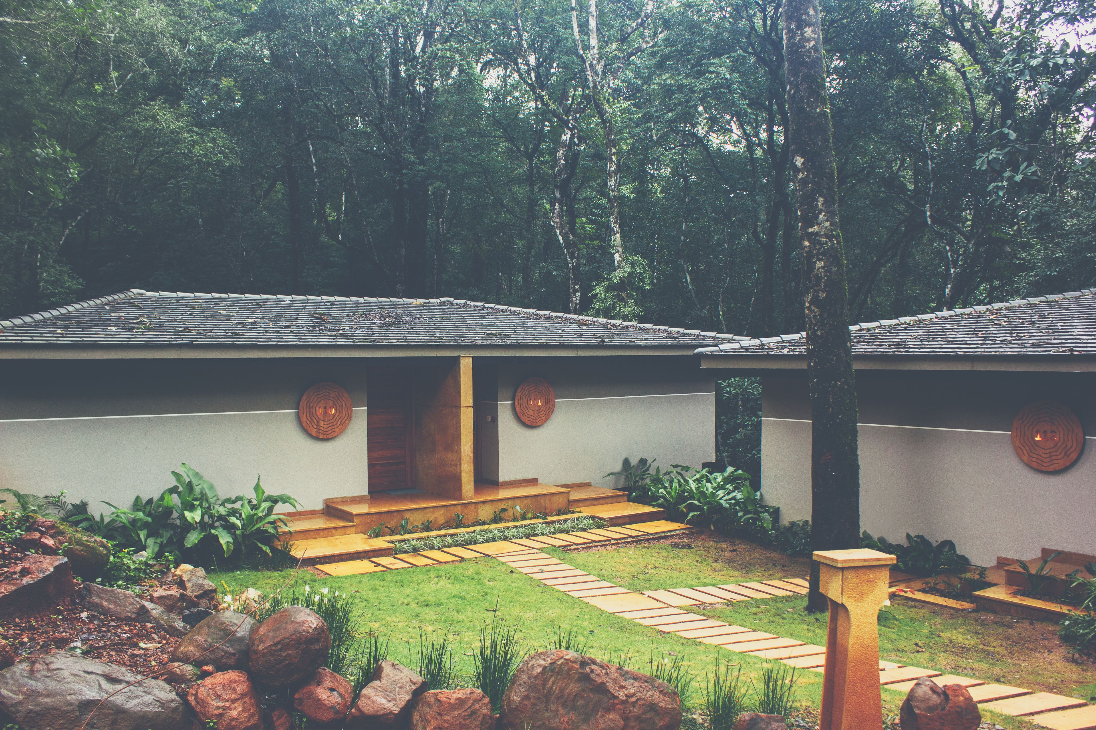 A modern building with a tiled roof, a wooden staircase leading to a door, and a garden with rocks and plants.