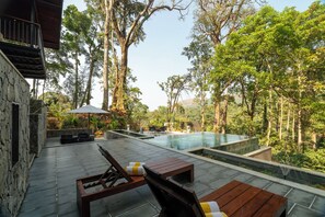 Une piscine avec vue sur les arbres, un bâtiment en pierre et du mobilier d’extérieur.