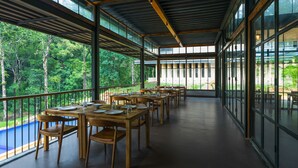 A spacious outdoor dining area with wooden tables and chairs, large windows, and a view of a forested area.