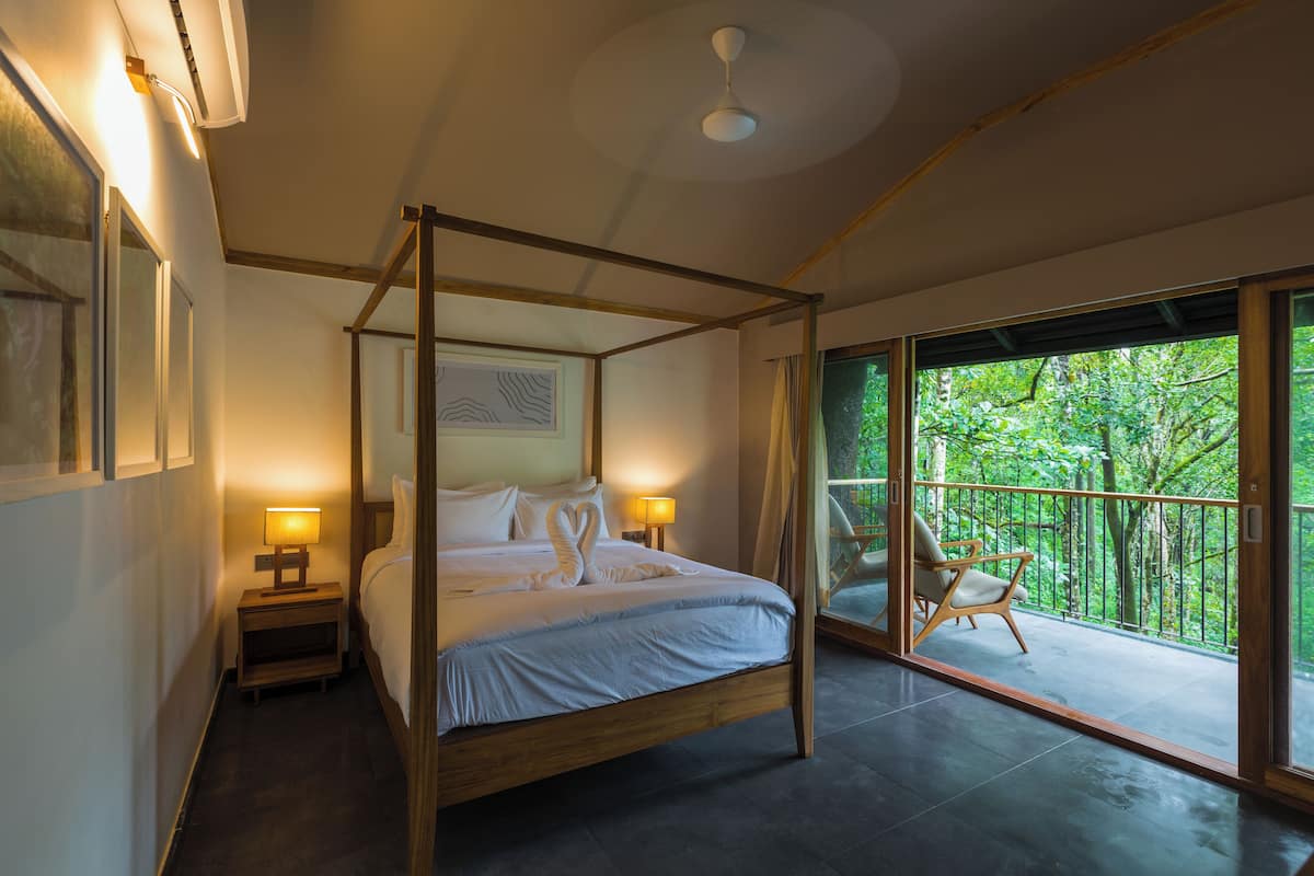Een hemelbed met houten frame, twee bedlampen en uitzicht op een balkon met een stoel.
