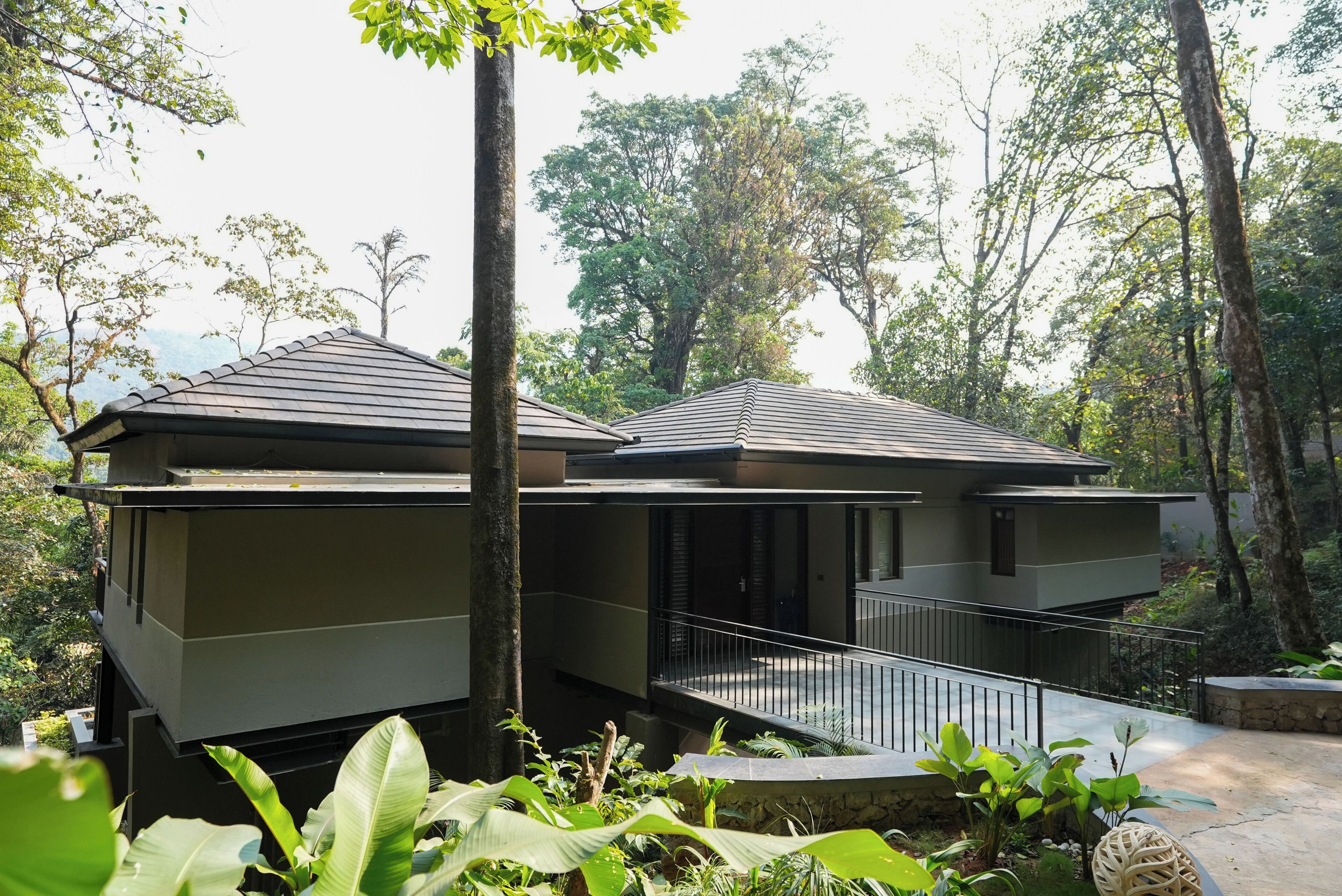 A modern two-story building with a balcony, surrounded by lush greenery.