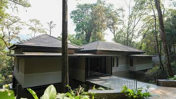 A modern two-story building with a balcony, surrounded by lush greenery.