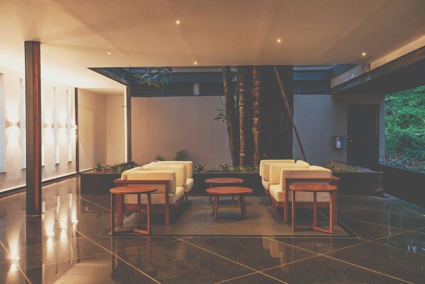 A modern lobby with a seating area featuring sofas and round tables, a polished floor, and a large window with a view of greenery. - Ayatana Coorg (Somvarpet)