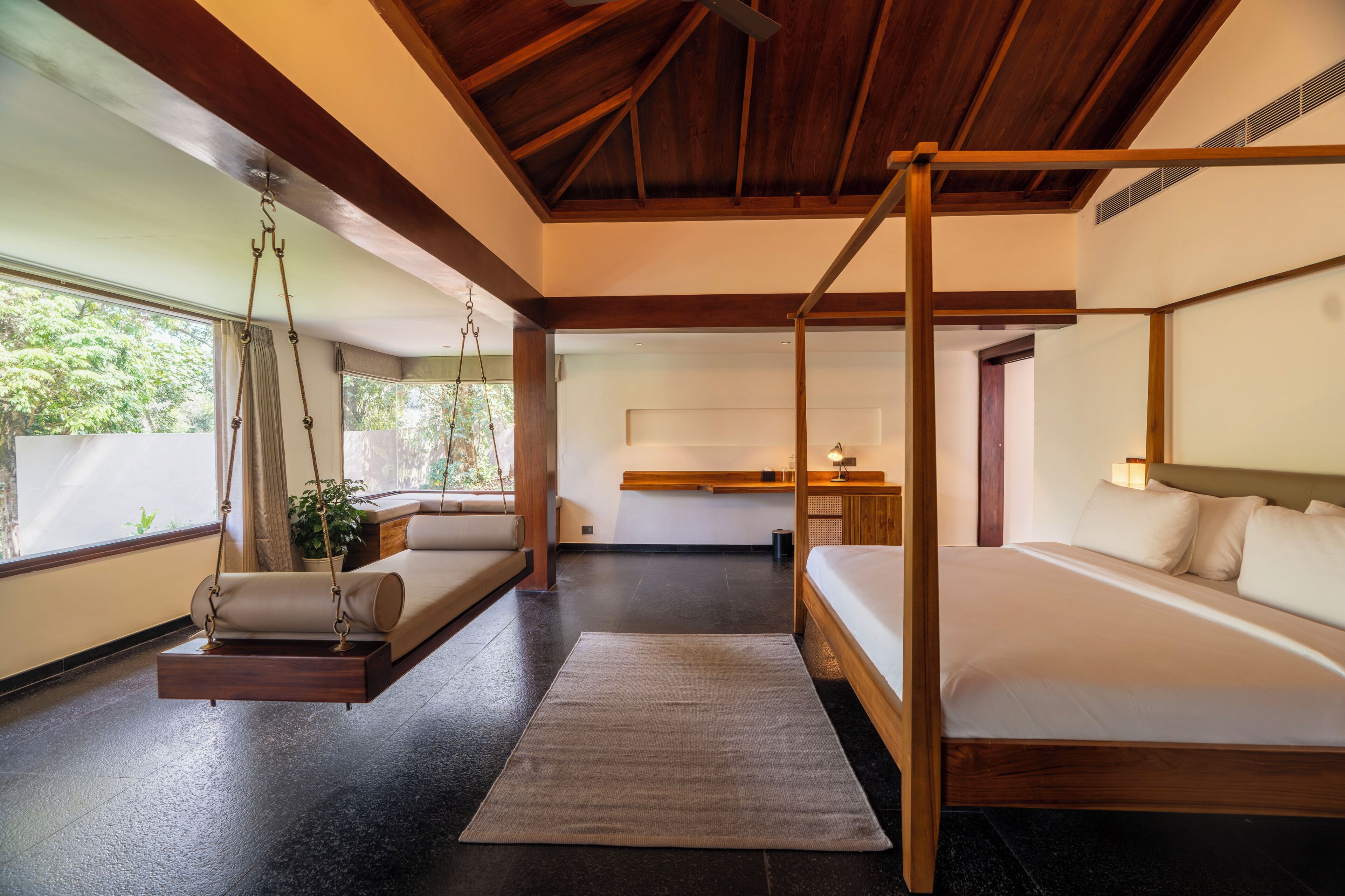 A bedroom with a four-poster bed, a hanging swing, a bedside table, and a view of the outdoors.