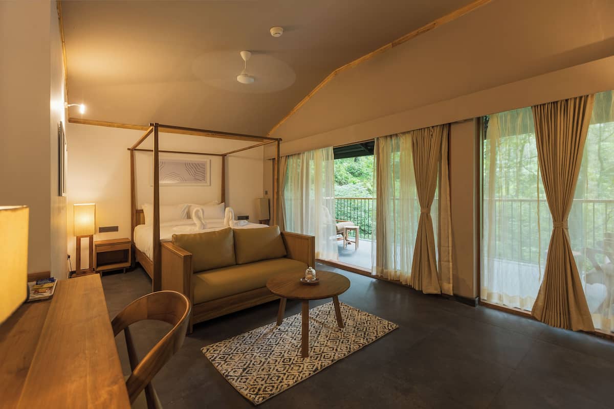 Een slaapkamer met een hemelbed, een bank, een klein tafeltje en uitzicht op de omgeving.