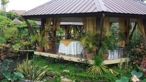 Un espacio al aire libre cubierto con una mesa dispuesta para comer, rodeado de abundante vegetación y plantas en macetas.