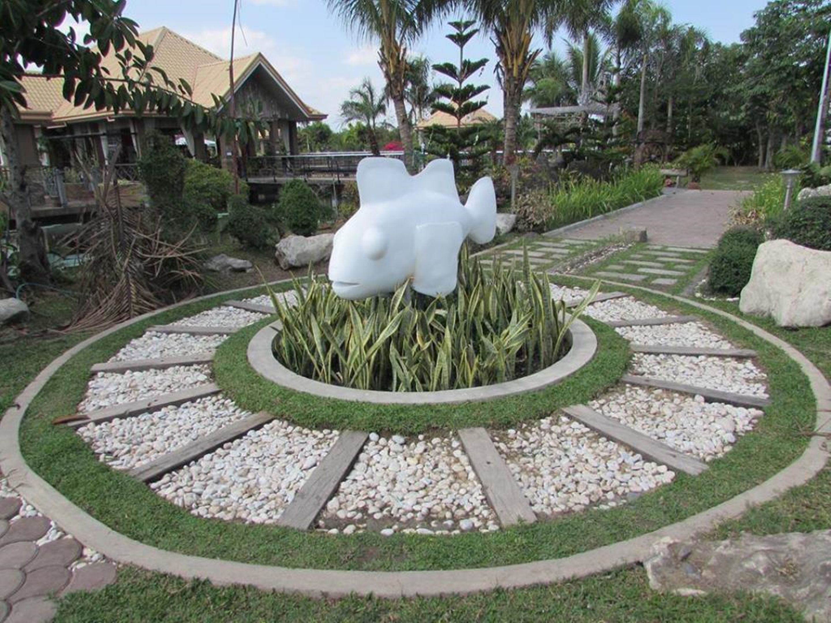 A garden with a central sculpture, surrounded by a circular pathway with gravel and grass.