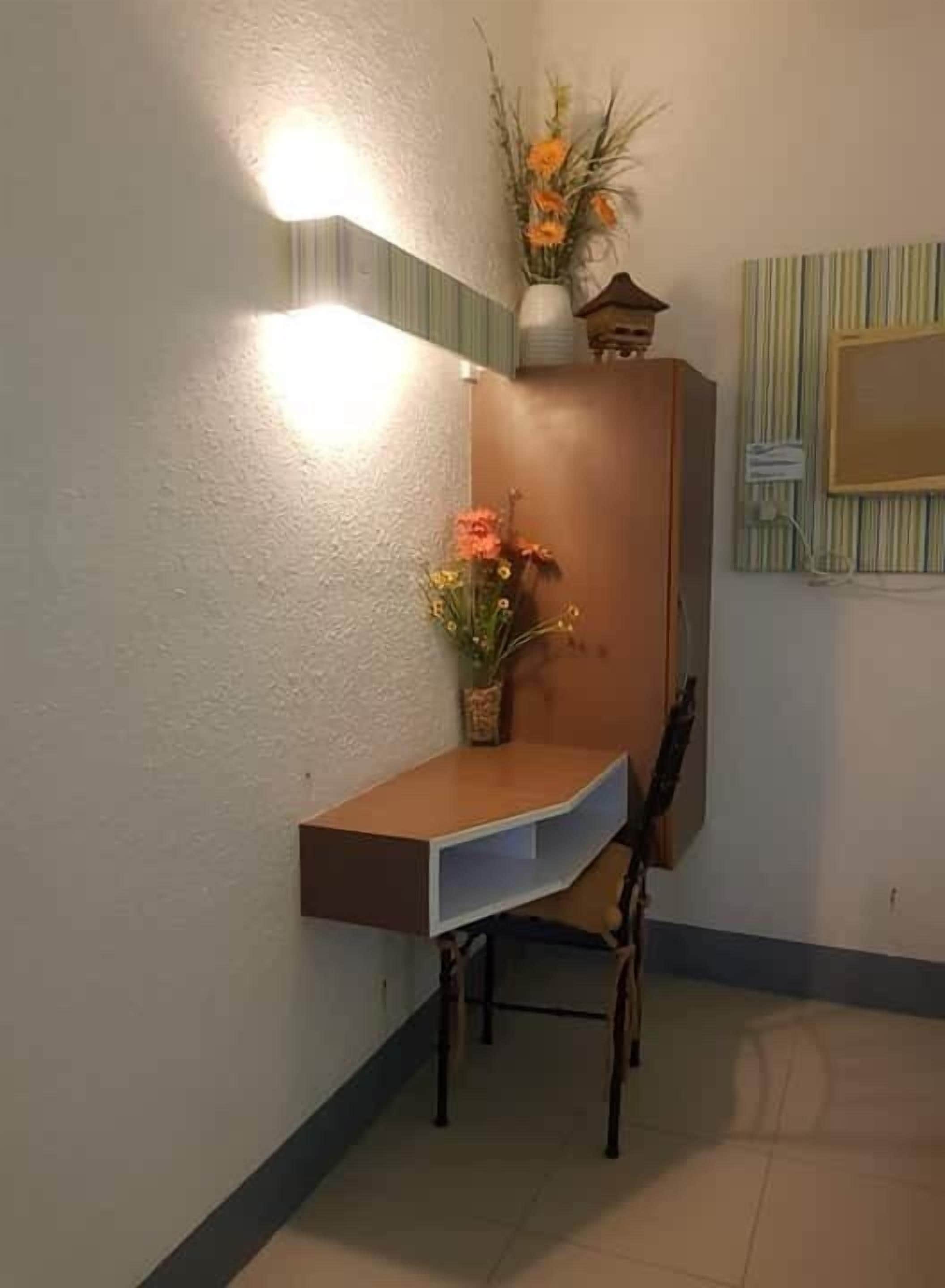 A corner desk with a chair, a vase with flowers, and a wall-mounted light fixture.