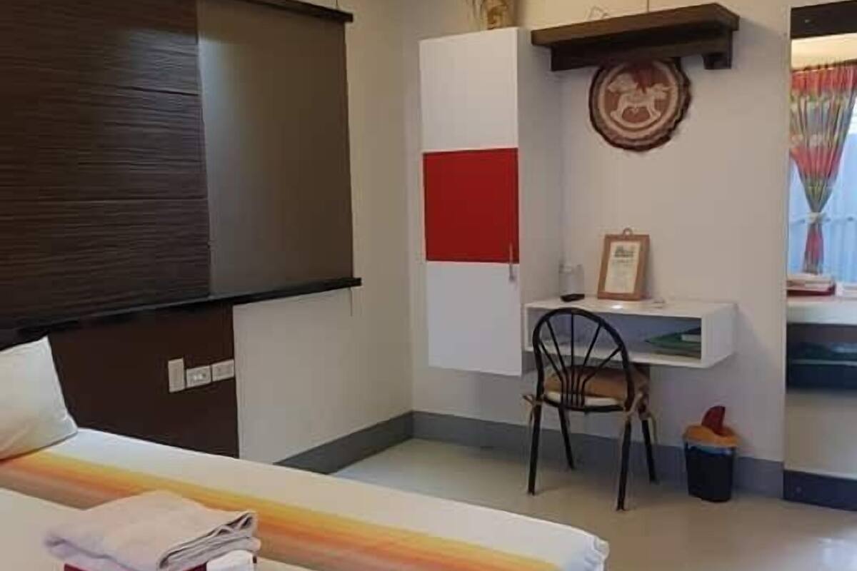 A hotel room with a bed, a desk, a chair, a small table, and a trash bin.