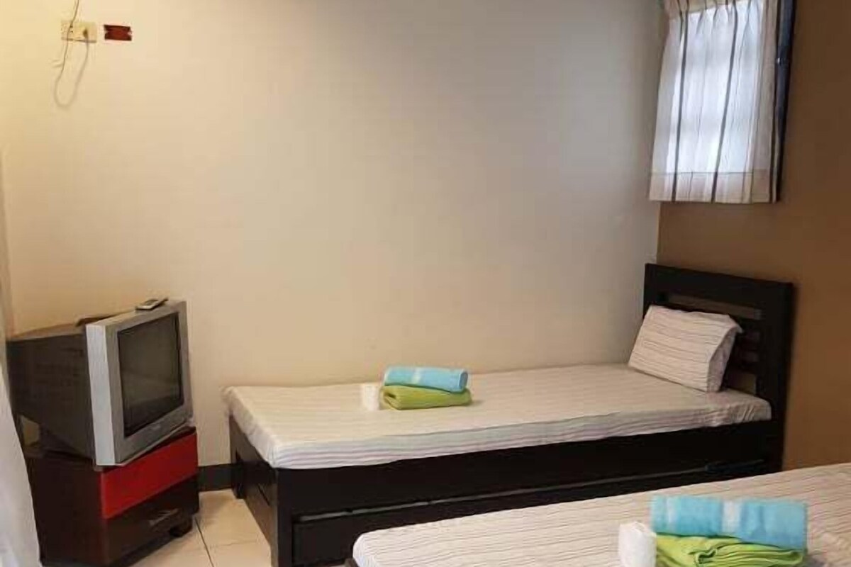 A small, clean room with two beds, a TV, and a window with curtains.