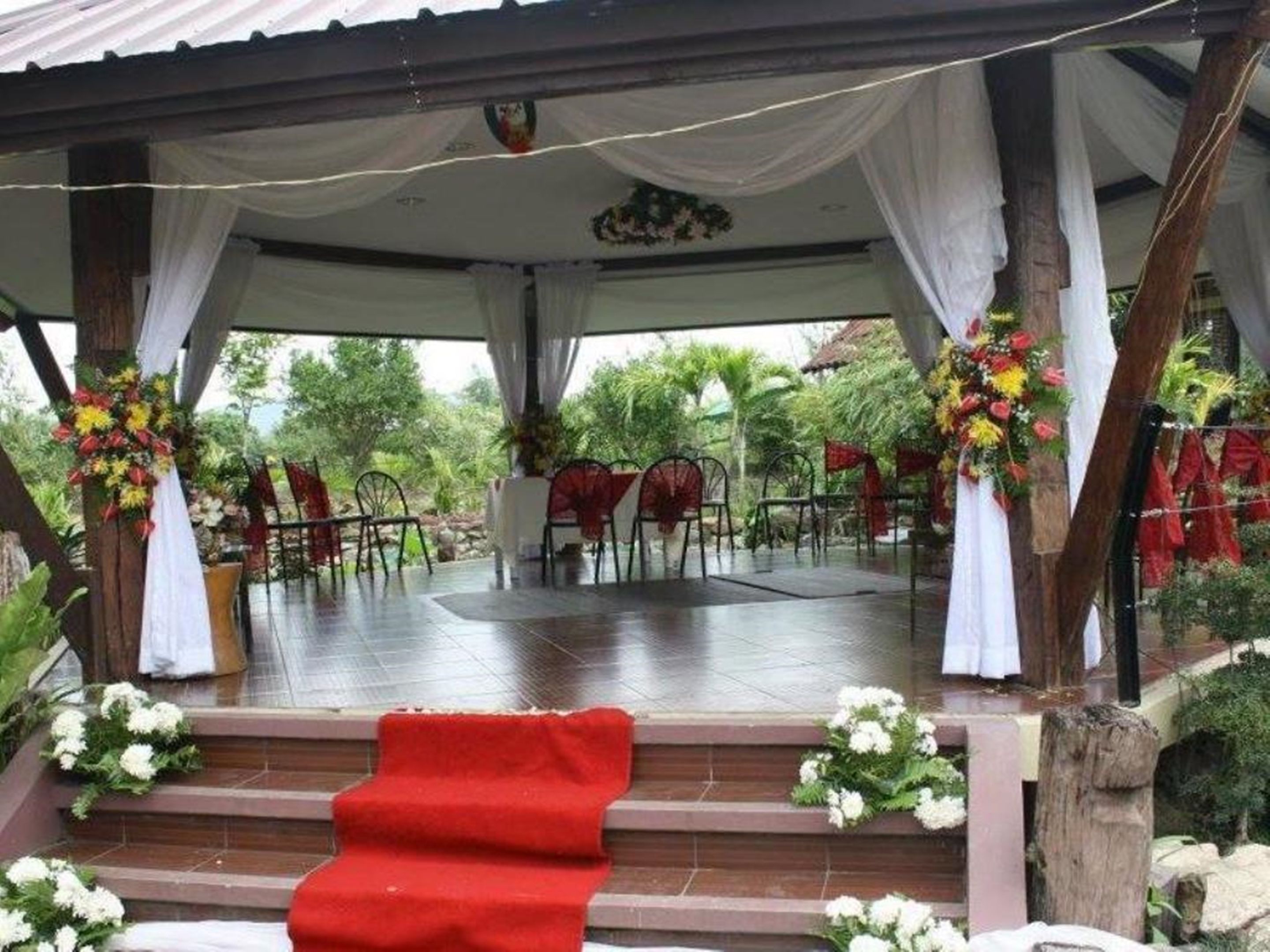Un espacio al aire libre techado con escenario, sillas y adornos florales.