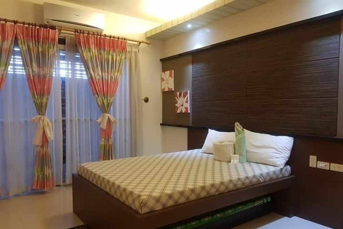A bedroom with a bed, curtains, a wall-mounted artwork, and a bedside table.