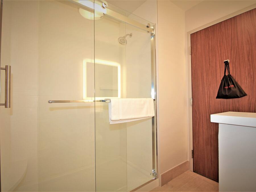 A modern bathroom with a glass shower enclosure, a wooden panel wall, and a white sink.