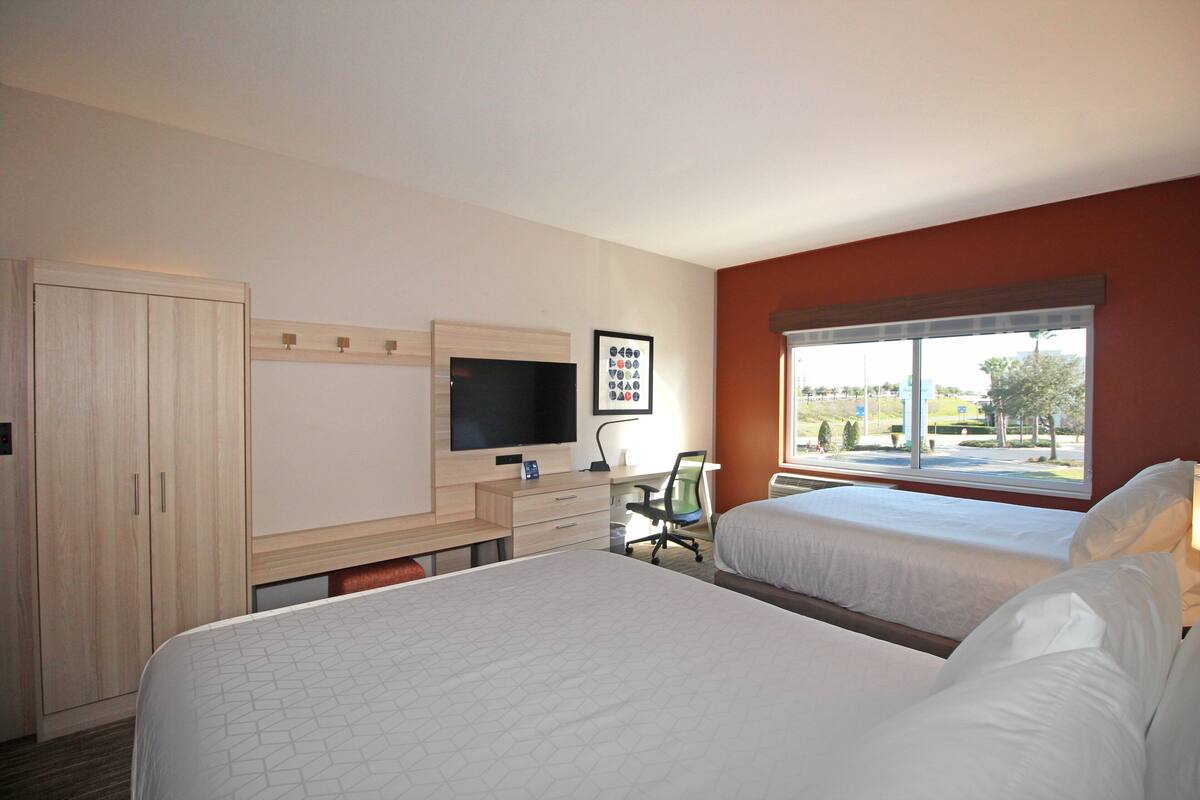 Une chambre d’hôtel avec deux lits, un bureau avec une chaise, une télévision et une fenêtre donnant sur l’extérieur.
