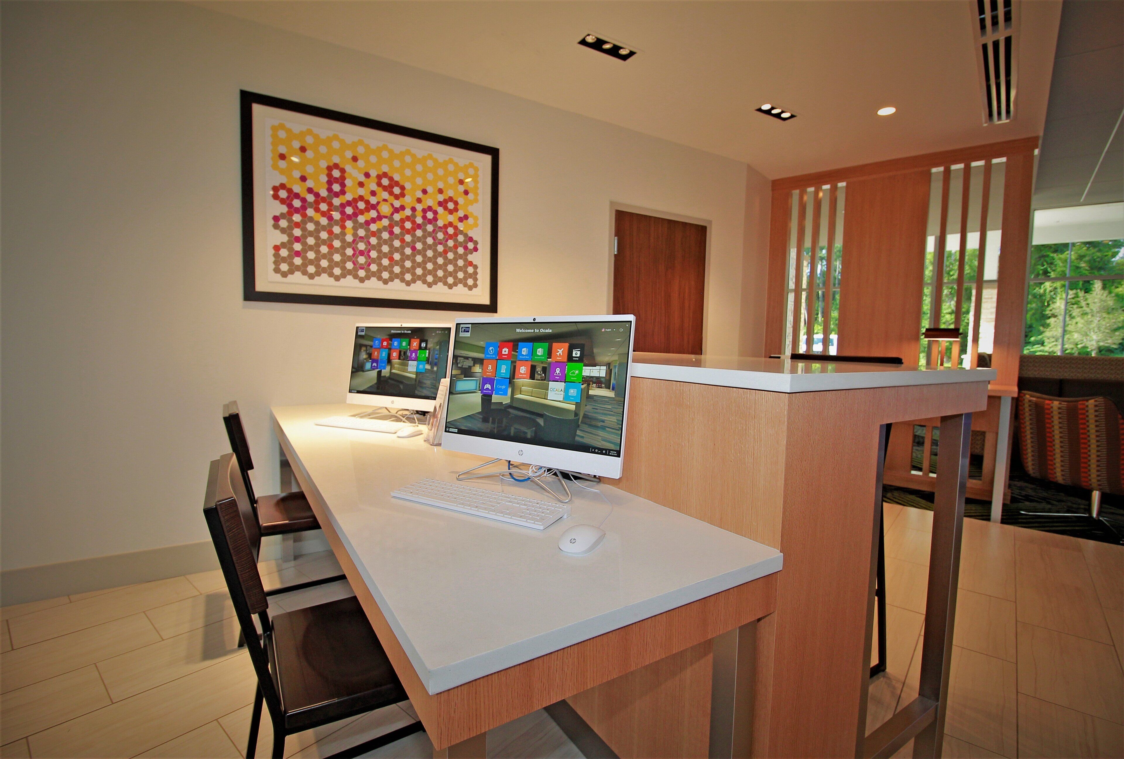 Un espacio de oficina moderno con dos computadoras de escritorio, una obra de arte abstracta enmarcada y un mostrador de recepción de madera.