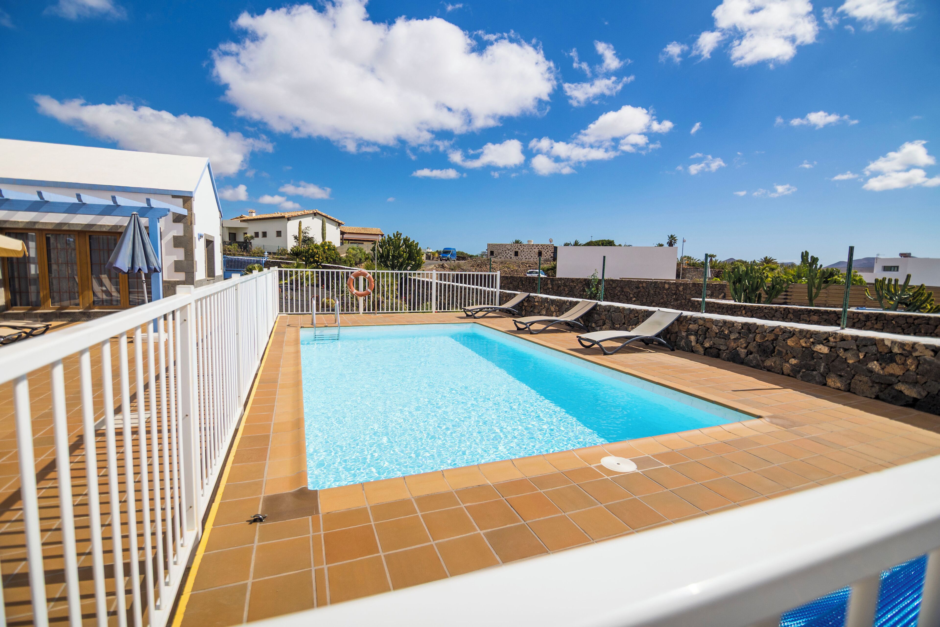 Una piscina en la azotea con barandilla blanca, un flotador salvavidas y un cielo azul despejado.