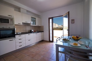 Una cocina moderna con armarios blancos, microondas y comedor con mesa de vidrio.