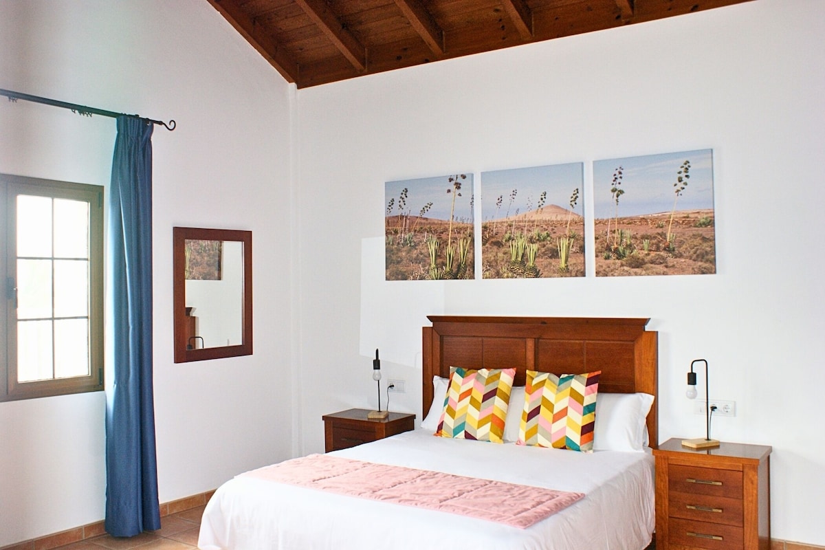 Un dormitorio con cama, mesita de noche, espejo, ventana con cortinas y decoración de temática desértica.