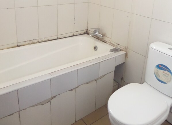A bathroom with a white bathtub, a white toilet, and white tiles on the walls.